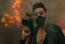 Man holding a gun with sunglasses, standing amid a fiery scene.