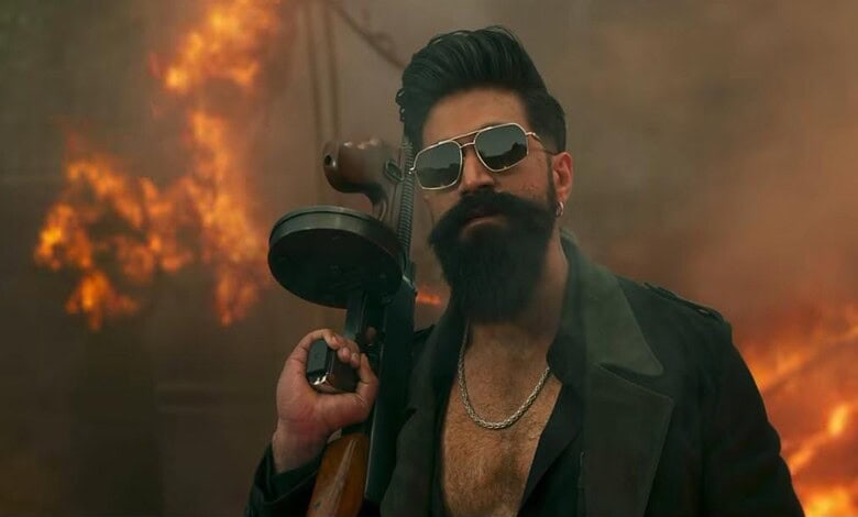 Man holding a gun with sunglasses, standing amid a fiery scene.