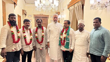 Group of politicians with garlands and traditional attire at an indoor event.