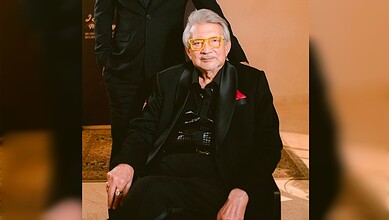 Rajan Lall in black suit with yellow glasses seated indoors at an event.