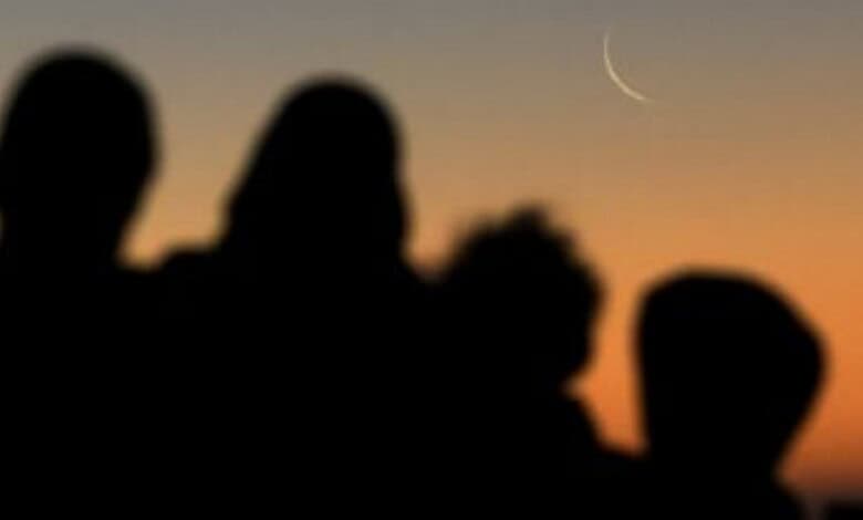 Silhouettes of people watching the crescent moon at sunset.