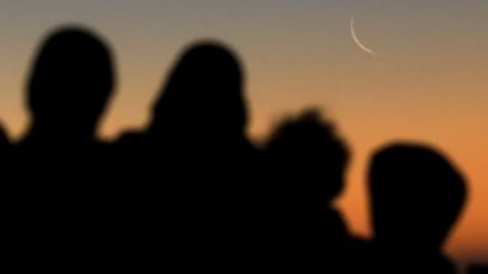 Silhouettes of people watching the crescent moon at sunset.