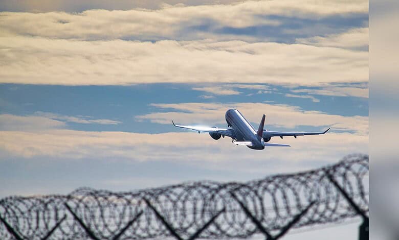 Image shows a plane in the sky above a barbed wire fence, representing themes of deportation and seeking safety.