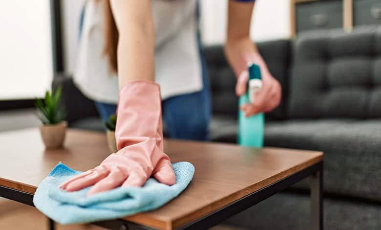 Domestic worker wiping a wooden coffee table with a cloth while holding a cleaning spray bottle.