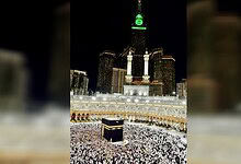 Night view of the Kaaba in Masjid al-Haram, Mecca, illuminated with city lights in the background.