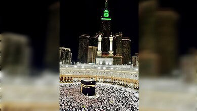 Night view of the Kaaba in Masjid al-Haram, Mecca, illuminated with city lights in the background.