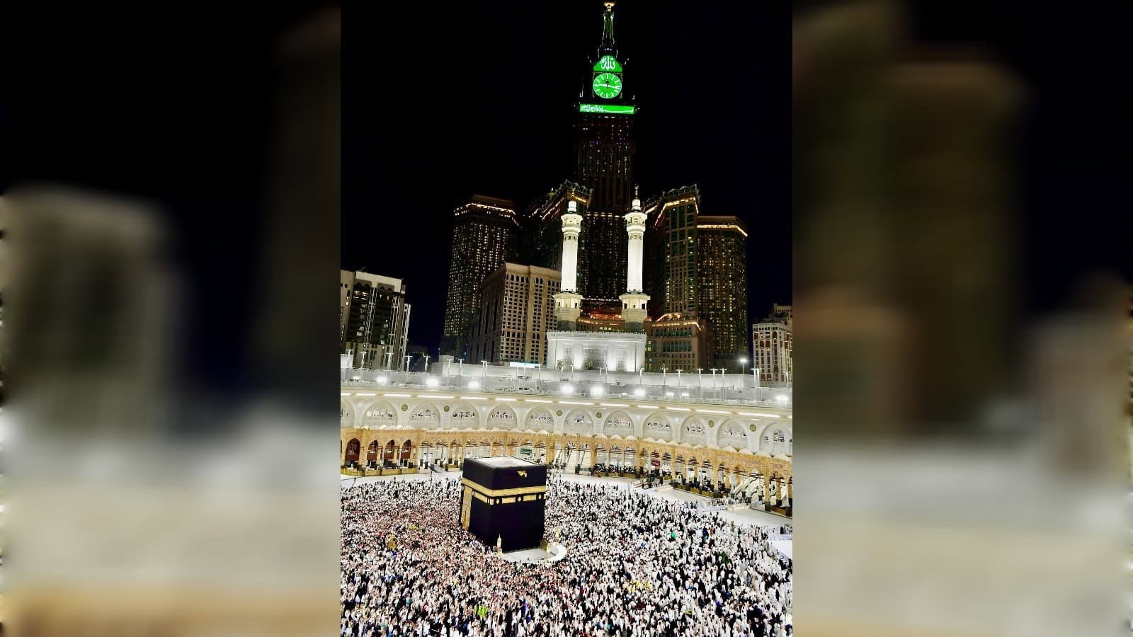 Night view of the Kaaba in Masjid al-Haram, Mecca, illuminated with city lights in the background.