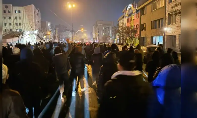 Large crowd gathered on a city street at night, illuminated by streetlights and building lights.