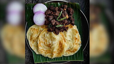 Delicious spicy beef served with crispy paratha and fresh onion slices on a banana leaf. Traditional Indi.
