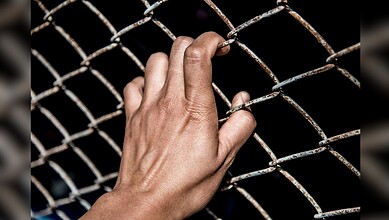 Hand gripping rusty wire fence, symbolising imprisonment or restriction.