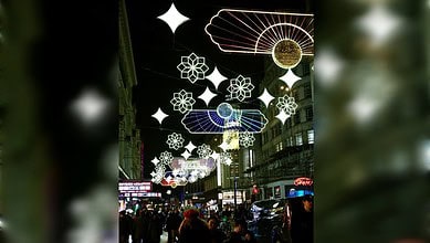 Colourful illuminated street decorations with stars and umbrellas in a lively urban setting.