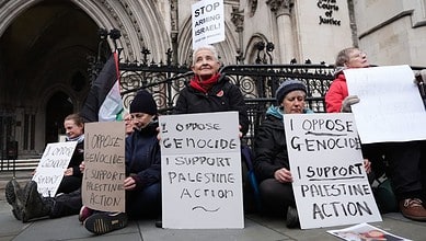 Palestine activists hold signs opposing genocide and supporting Palestinian action outside the High.