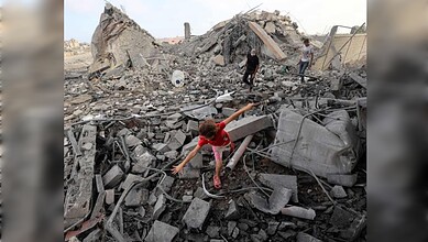 Palestinian girl walks across debris as civilians inspect the rubble of a building destroyed in an Israeli air strike in Bureij refugee camp, central Gaza Strip.