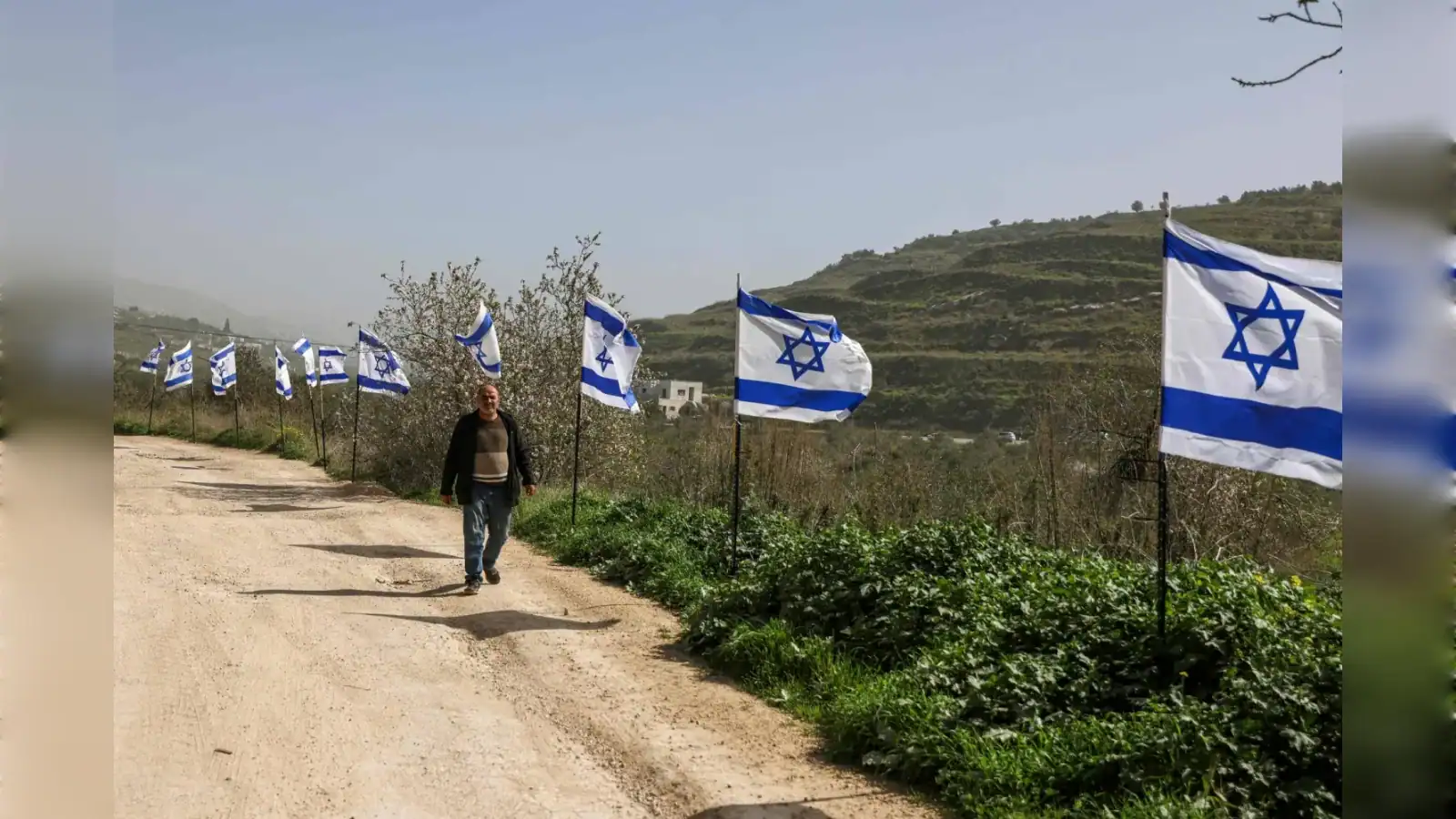 Palestinian man walks past Israeli flags near Al-Masoudiya railway site in occupied West Bank.