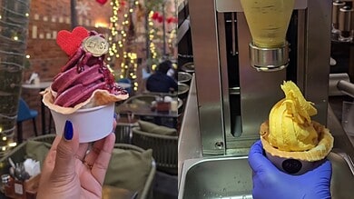 Up of a hand holding a pink and purple ice cream with a heart-shaped decoration.