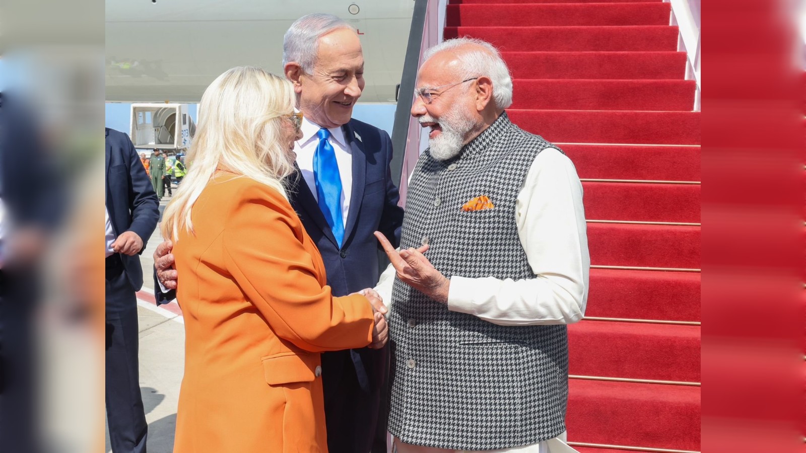 Prime Minister Modi greets officials on arrival in Israel, with a red carpet and stairs in the background.