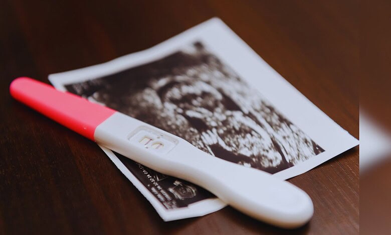 Image shows a Pregnancy test and ultrasound image on wooden surface