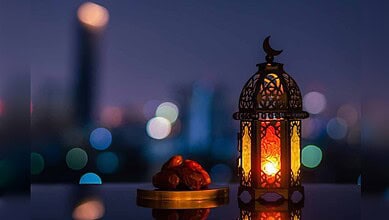 Lantern with intricate design and glowing light, placed beside dates on a balcony at dusk.