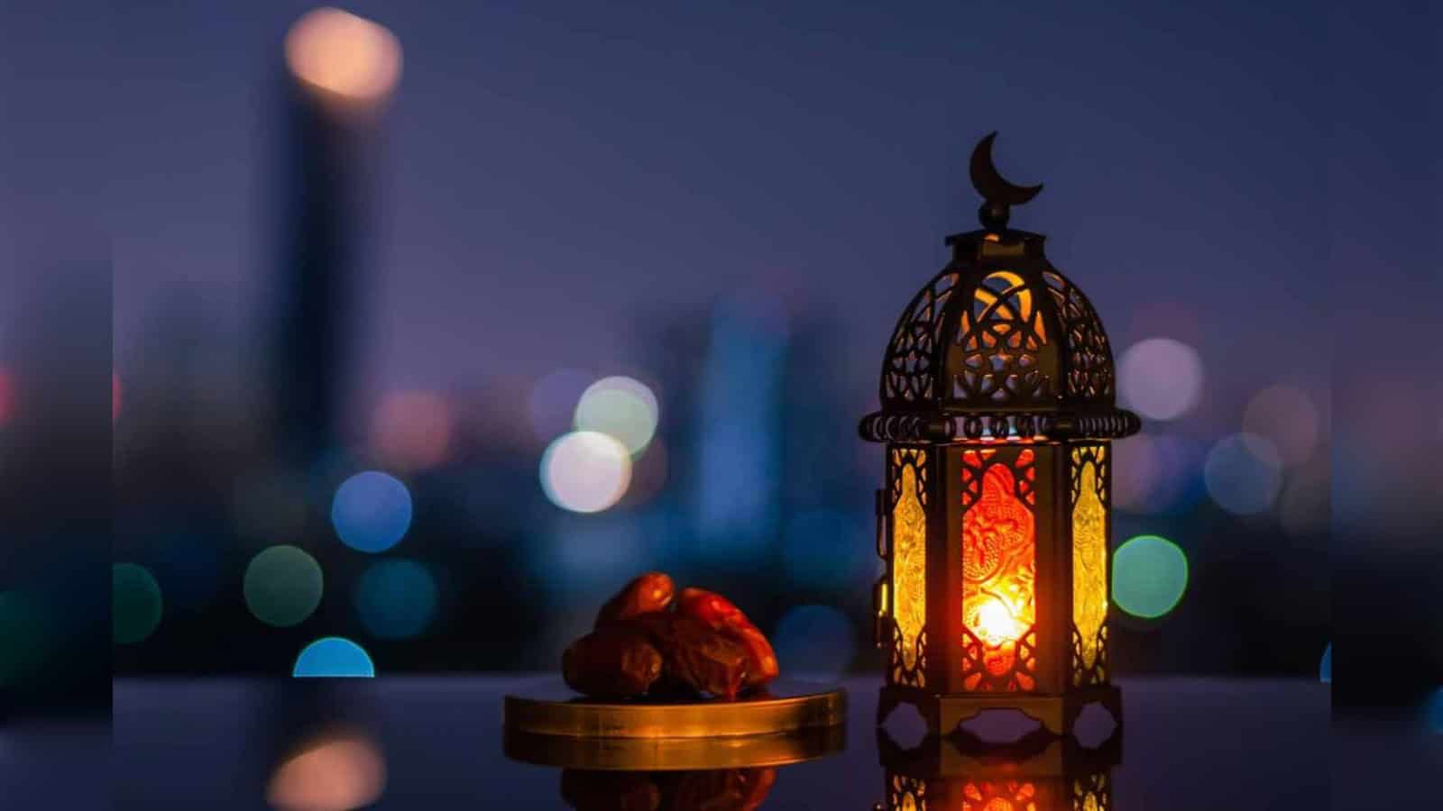 Lantern with intricate design and glowing light, placed beside dates on a balcony at dusk.
