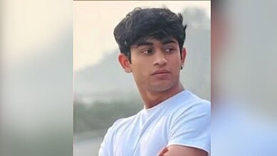 Young man with black hair in a white t-shirt looking away outdoors.