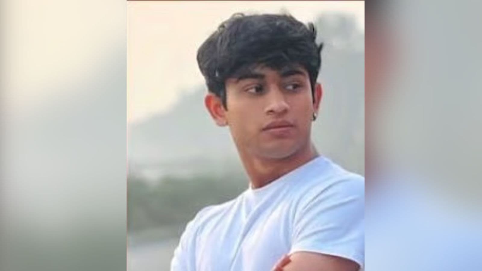 Young man with black hair in a white t-shirt looking away outdoors.