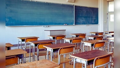 Image shows Empty classroom with wooden desks and blue chalkboards