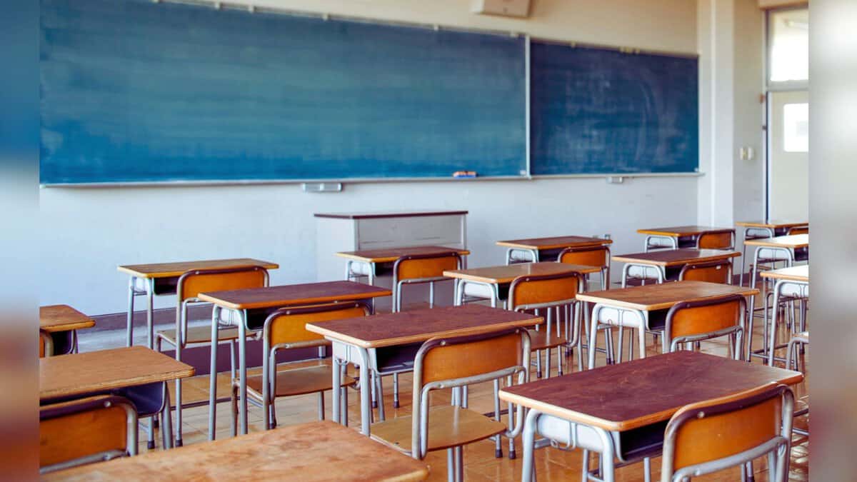 Image shows Empty classroom with wooden desks and blue chalkboards