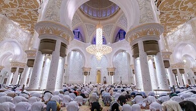 Worshippers perform congregational prayer inside Sheikh Zayed Grand Mosque in Abu Dhabi beneath ornate chandeliers and white marble arches.