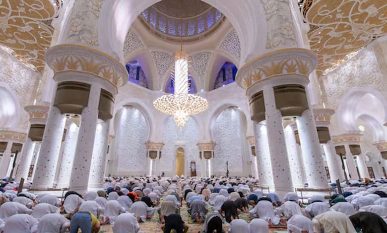 Worshippers perform congregational prayer inside Sheikh Zayed Grand Mosque in Abu Dhabi beneath ornate chandeliers and white marble arches.