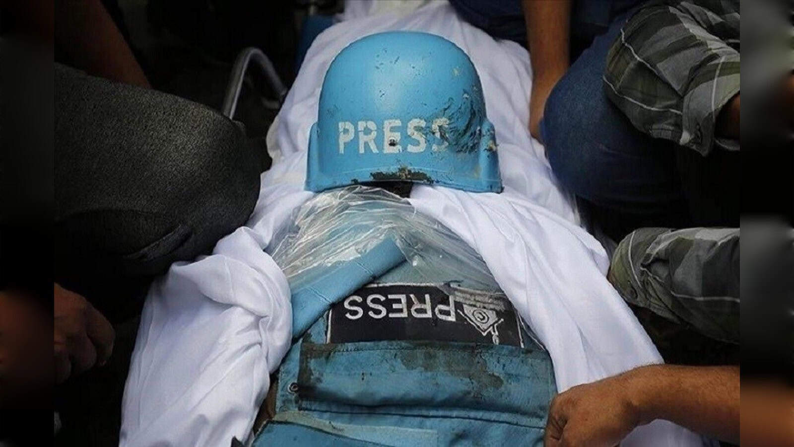 Protester wearing a blue helmet and press badge during a demonstration, surrounded by people.