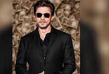 SRK with sunglasses in front of money background, reflecting his financial comeback after losses.