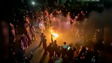 Protesters gather in a street in Tehran, dancing and cheering around a bonfire during a night-time demonstration.