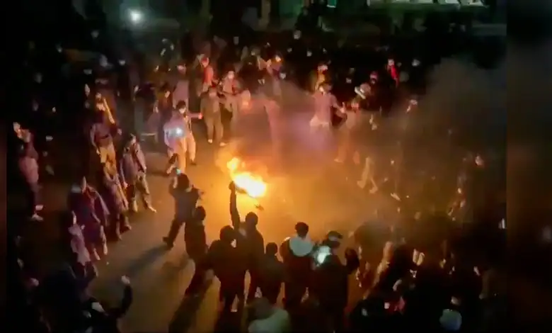 Protesters gather in a street in Tehran, dancing and cheering around a bonfire during a night-time demonstration.