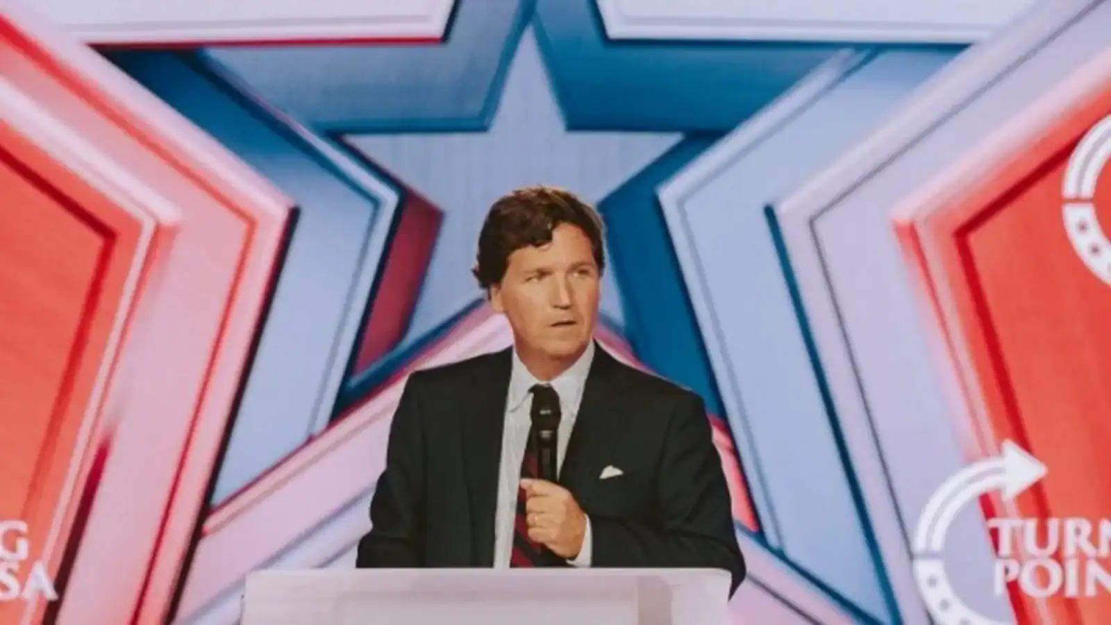 Podcast host Tucker Carlson speaks at a podium during Turning Point’s AmericaFest conference in Phoenix, Arizona.