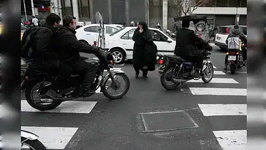 A woman crosses a street as motorbikes pass in central Tehran, Iran.