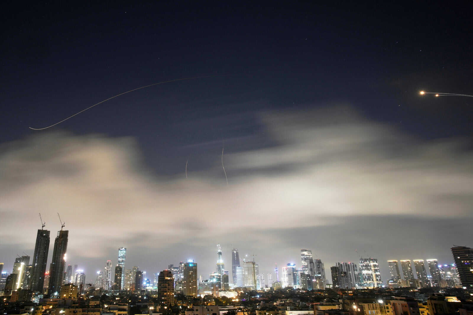 Night city skyline with tall buildings and aircraft trails in the sky.