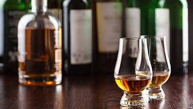Alcoholic drinks served in glasses on a bar counter with bottles behind.