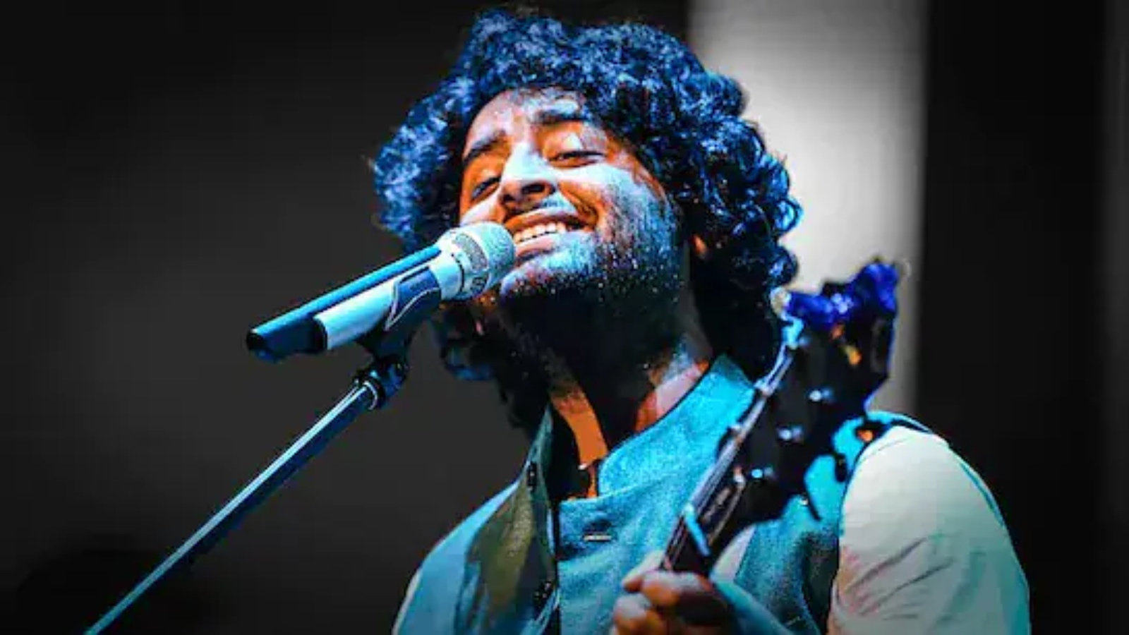 A singer with curly hair passionately performs with a microphone and guitar at The Siasat Daily event, sh.