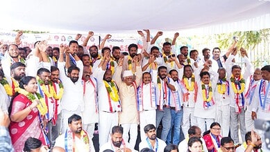 Protesters raising fists and cheering at a political rally in India, with banners and flags in the backgr.