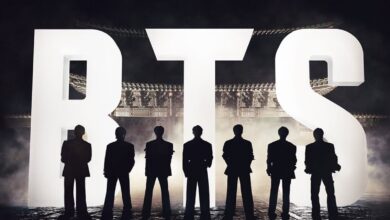 K-pop stars standing on stage during a comeback event, silhouetted against bright lights.