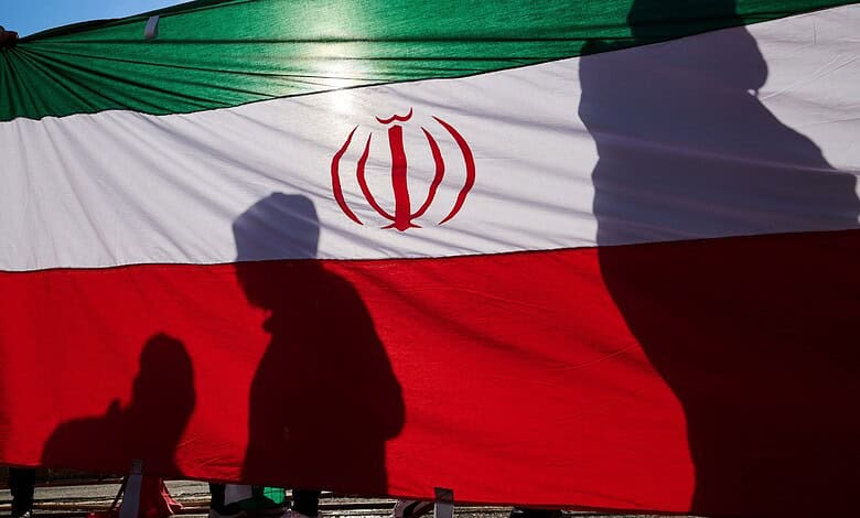 Iranian flag with silhouettes of people at a public gathering.