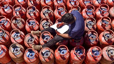 A worker sits over LPG cylinders during distribution at a gas agency.