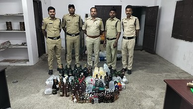 Police officers with seized bottles of alcohol in a room.
