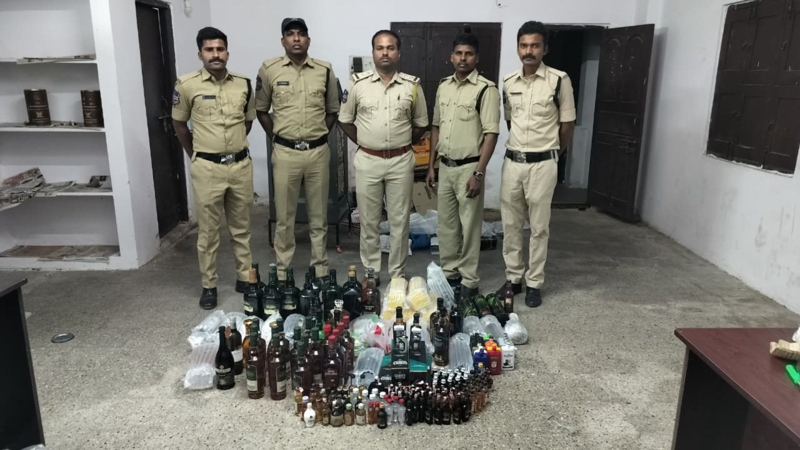 Police officers with seized bottles of alcohol in a room.
