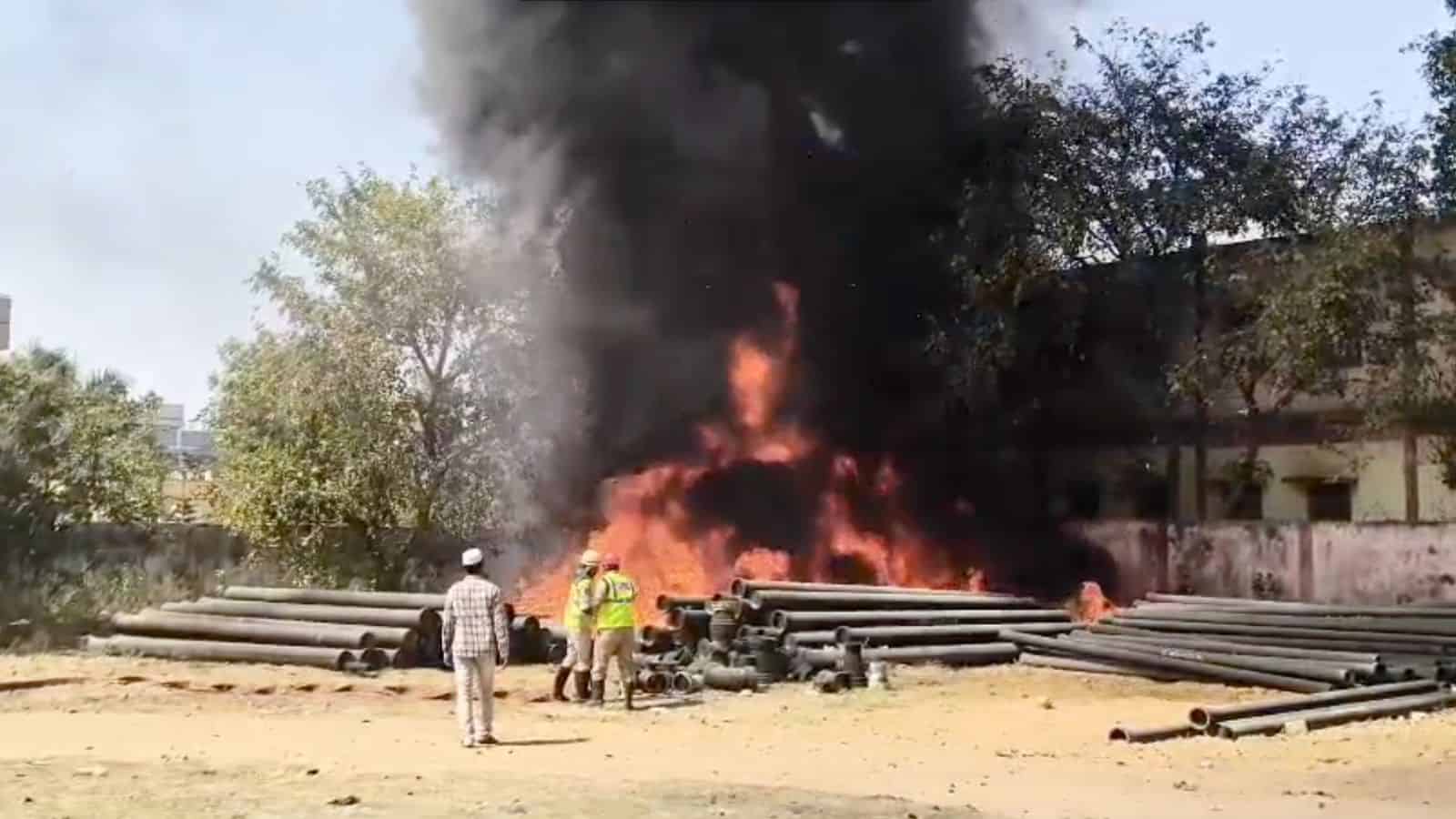 Fire and smoke at construction site with workers and onlookers nearby.