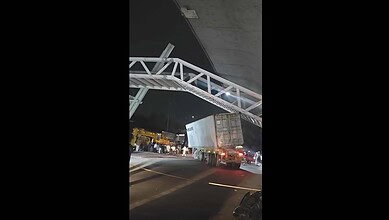 Large truck trapped beneath a construction walkway on a busy Hyderabad street at night.