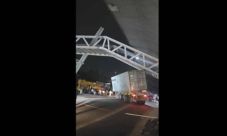 Large truck trapped beneath a construction walkway on a busy Hyderabad street at night.