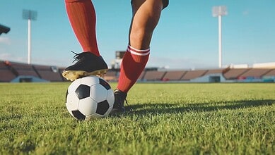Close-up of soccer players' legs and a ball on the field, with stadium in background, during match postpo.