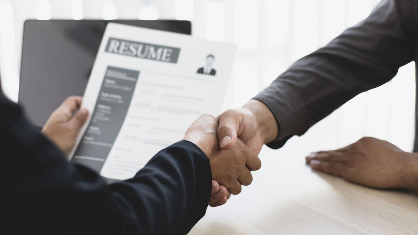 Handshake over a resume during a job interview in an office setting.