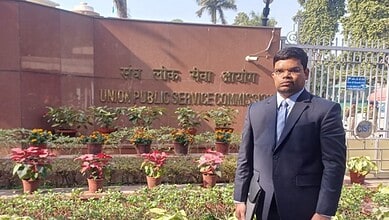 Man in formal suit standing outside Union Public Service Commission building in India.